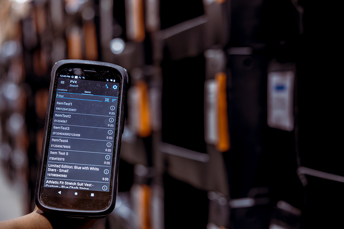 A warehouse worker’s hand is holding an Android mobile device displaying a warehouse management system (WMS) for multichannel ecommerce.
